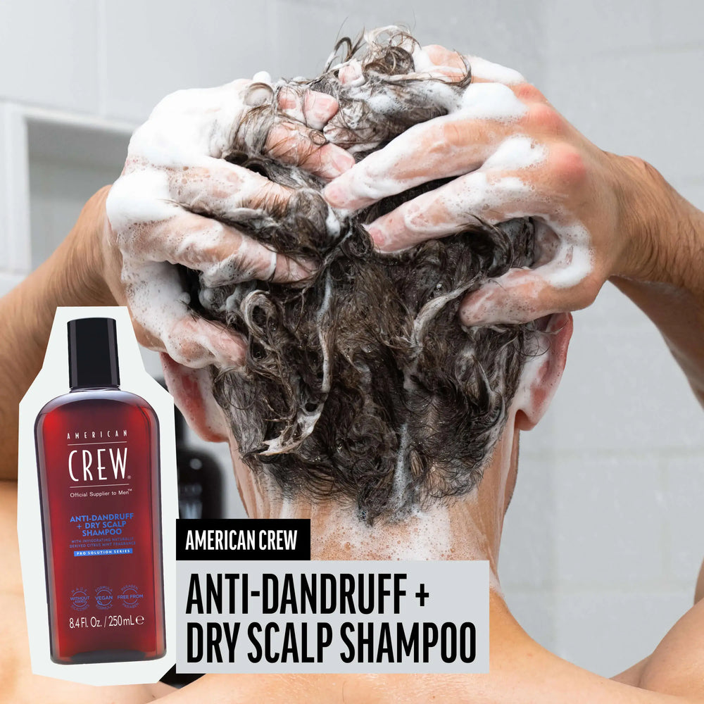 Man washing hair with American Crew Anti-Dandruff + Dry Scalp Shampoo, hair lathered and foamy, while product render and name are placed on the lower third of image.