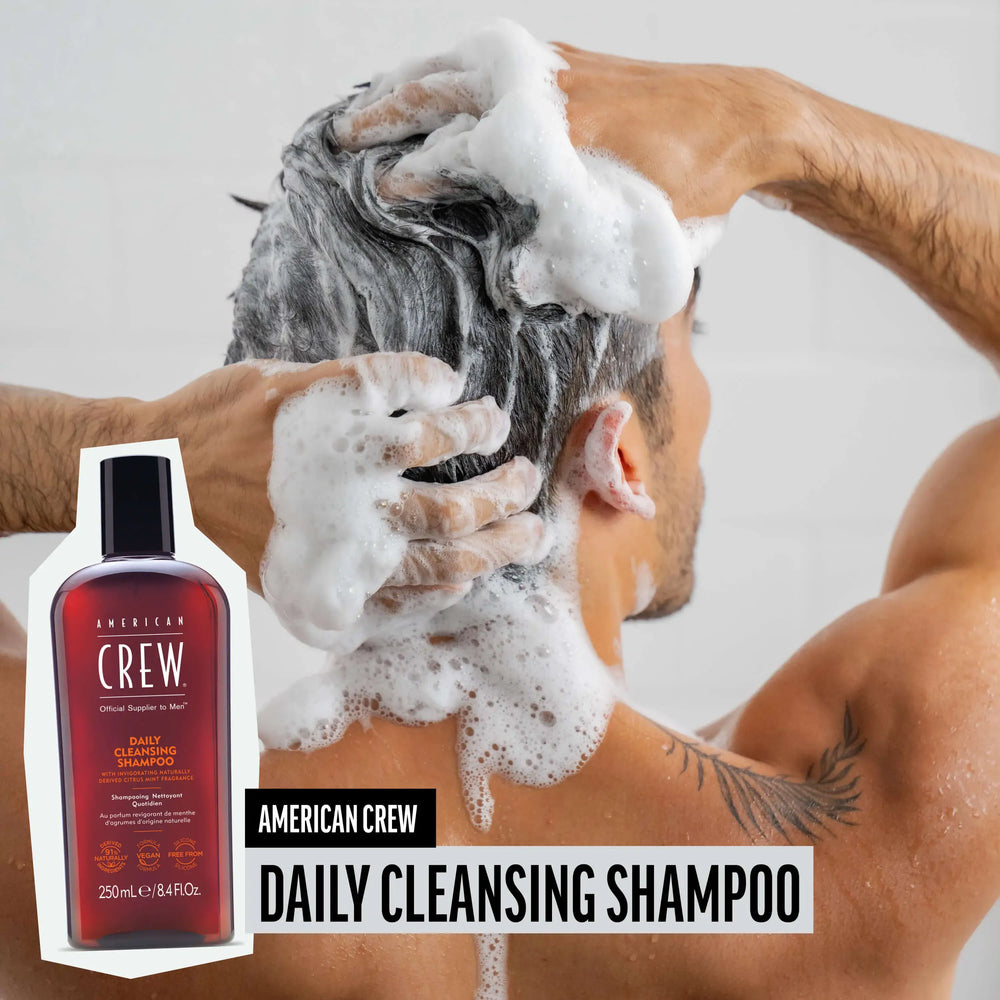 Man washing hair with American Crew Daily Cleansing Shampoo, hair lathered and foamy, while product render and name are placed on the lower third of image.