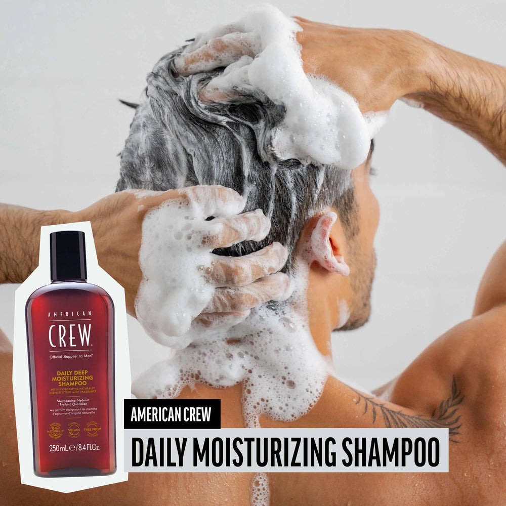 Man washing hair with American Crew Daily Deep Moisturizing Shampoo, hair lathered and foamy, while product render and name are placed on the lower third of image.