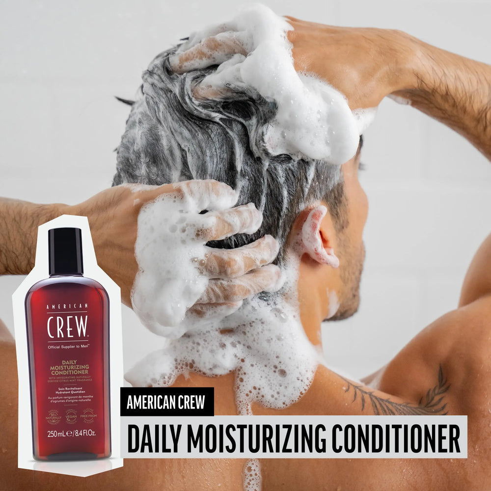 Man washing hair with American Crew Daily Moisturizing Conditioner, hair lathered and foamy, while product render and name are placed on the lower third of image.
