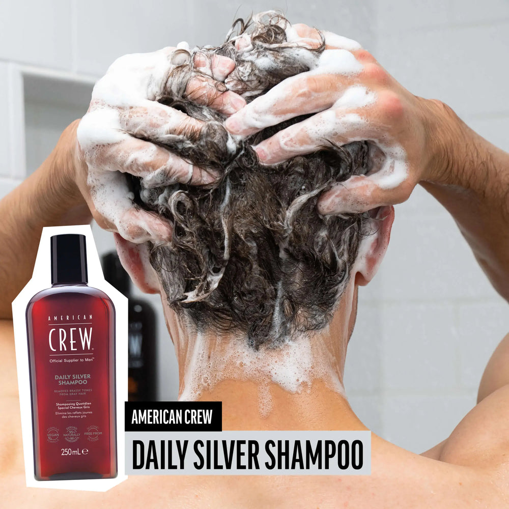 Man washing hair with American Crew Silver Shampoo, hair lathered and foamy, while product render and name are placed on the lower third of image.