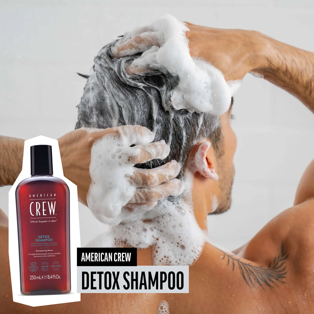 Man washing hair with American Crew Daily Detox Shampoo, hair lathered and foamy, while product render and name are placed on the lower third of image.