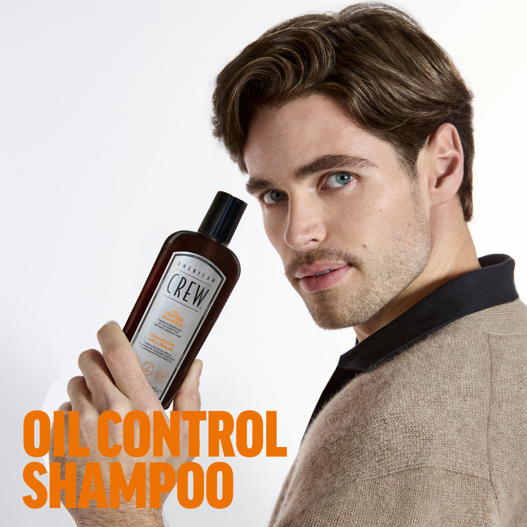 Charly Poirier holding a bottle of American Crew Oil Control Shampoo while wearing a tweed jacket with a black collar against a white background