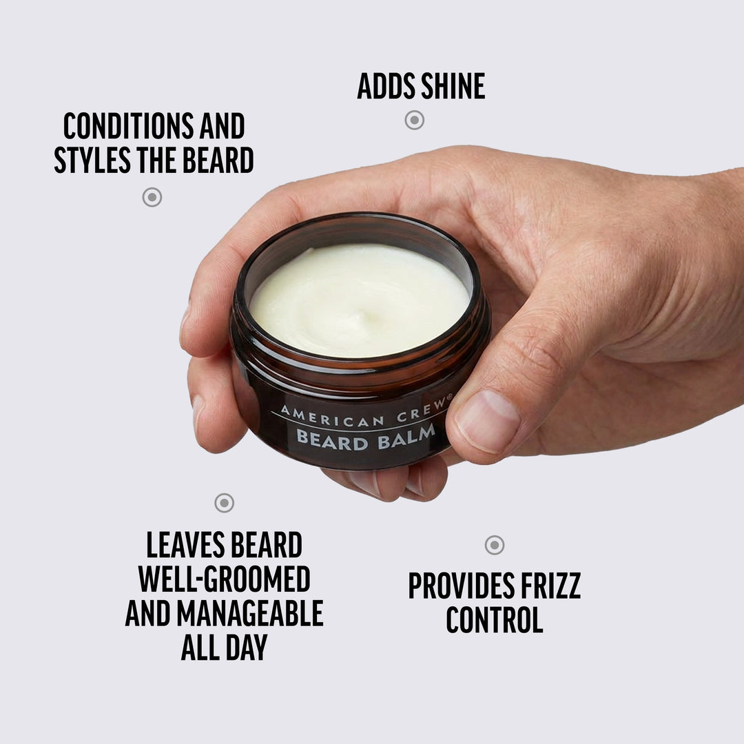Hand holding a jar of American Crew Beard Balm with text highlighting its benefits on a white background.
