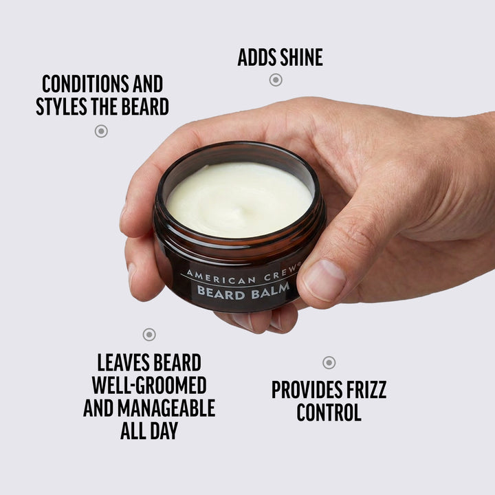 Hand holding a jar of American Crew Beard Balm with text highlighting its benefits on a white background.