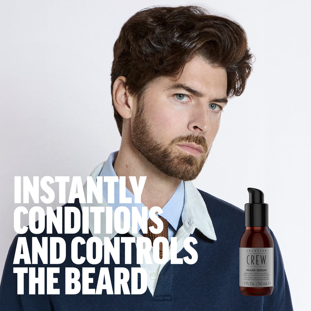 Model Ferrari Calderon is sporting a full beard, wearing a blue sweater and blue shirt with an overlay of American Crew Beard Serum next to the text "Instantly conditions and controls the beard". 