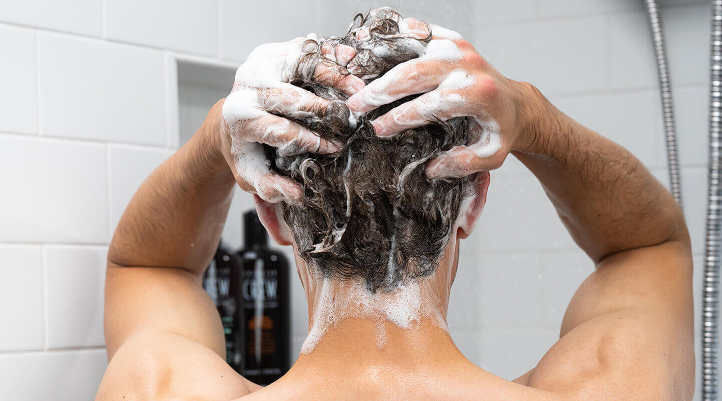 Chase Hamilton washing hair with American Crew shampoo in a bathroom.
