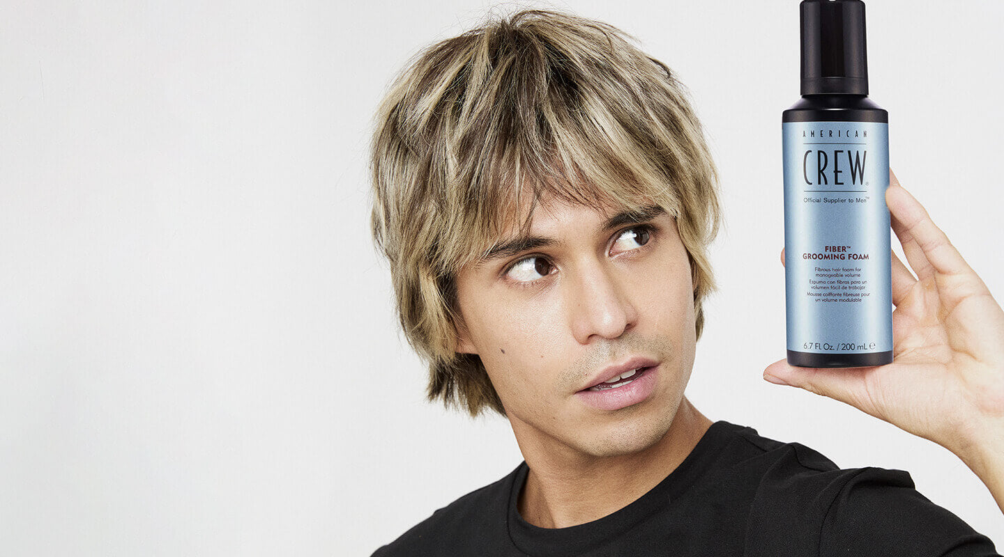 Manuel holding a bottle of American Crew Fiber Grooming Foam against a white background
