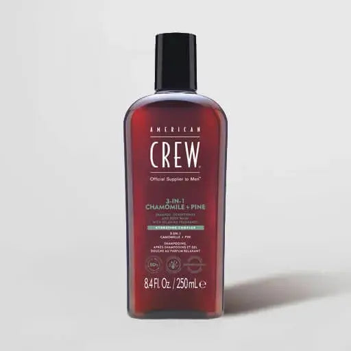 A bottle of American Crew 3-in-1 Chamomile + Pine hair care product with a black cap and dark reddish-brown bottle, shown on a light gray background.