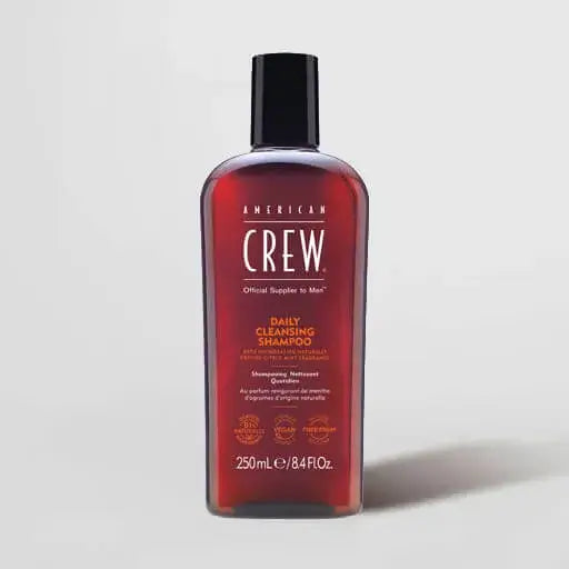 A bottle of American Crew Daily Cleansing Shampoo with a black cap and a dark red translucent bottle, shown on a light gray background.