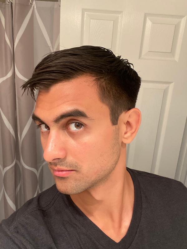 Profile Image of American Crew Fiber Cream Reviewer Anonymous, with styled hair, and a black v-neck shirt in his bathroom.