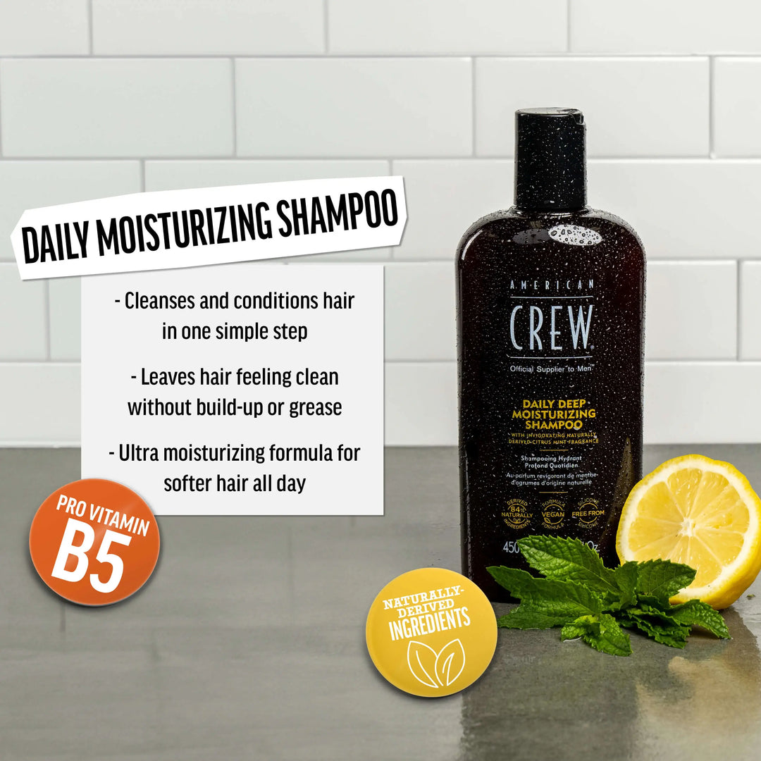 American Crew Daily Deep Moisturizing Shampoo bottle with lemon and mint leaves on a tiled background. Text callout says "Cleanses and conditions hair in one simple step. Leaves hair feeling clean without build-up or grease. Ultra moisturizing formula for softer hair all day". 