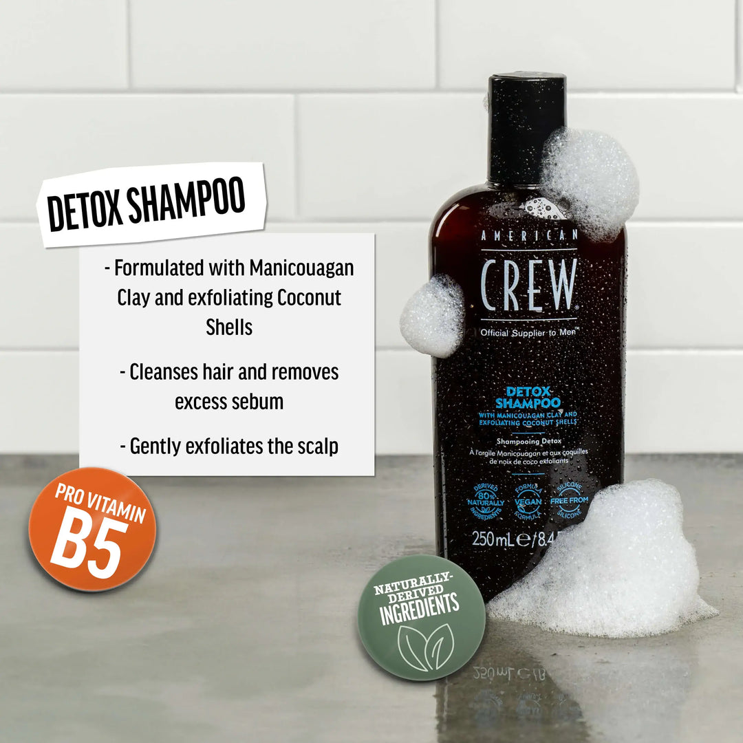 American Crew Detox Shampoo bottle on a bathroom shelf against a tiled background. Text callout says "Formulated with Manicouagan Clay and exfoliating Coconut Shells. Cleanses hair and removes excess sebum. Gently exfoliates the scalp".