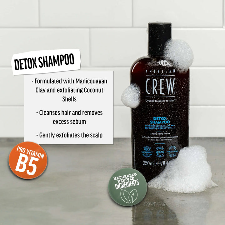 American Crew Detox Shampoo bottle on a bathroom shelf against a tiled background. Text callout says "Formulated with Manicouagan Clay and exfoliating Coconut Shells. Cleanses hair and removes excess sebum. Gently exfoliates the scalp".